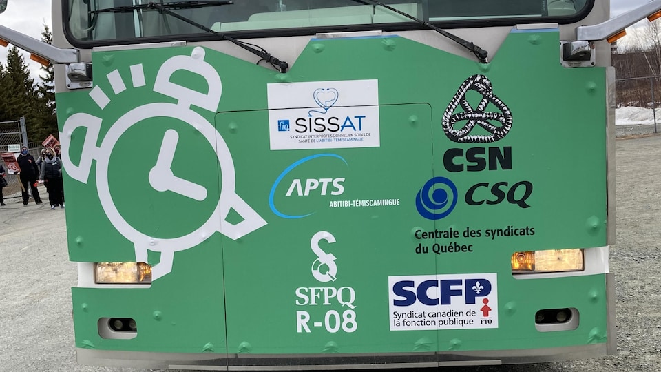 Les logos des syndicats des travailleurs de la fonction publique sont collés sur un autobus. Un réveille-matin s'y trouve aussi.