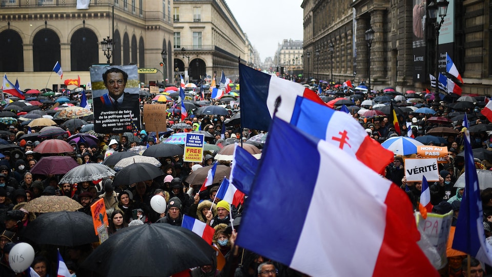 Une immense foule portant pancartes, drapeaux et parapluies est réunie.