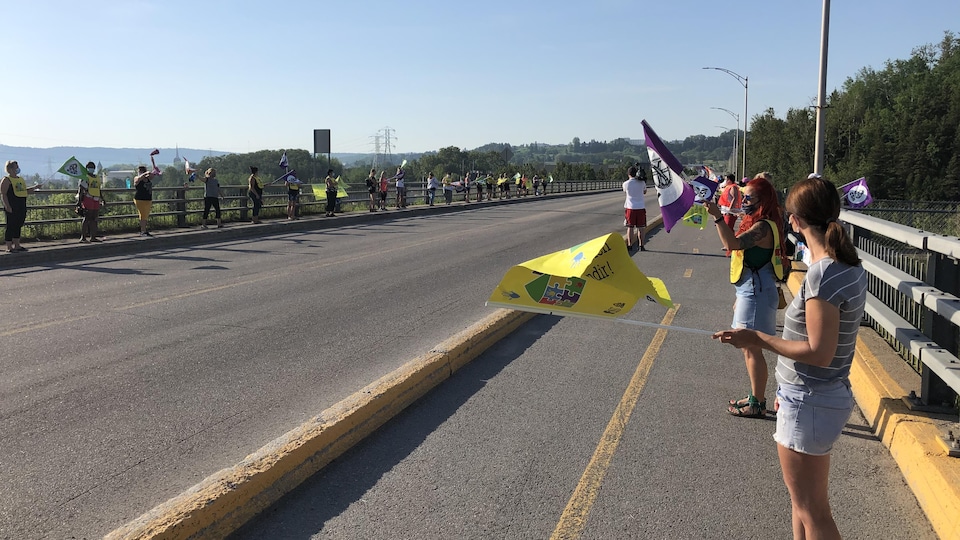 Des éducatrices se tiennent chaque côté du pont avec des drapeaux.