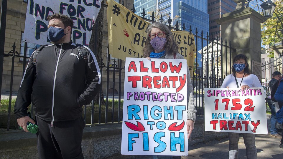 Des gens portant des masques et tenant des pancartes manifestent en solidarité avec les pêcheurs micmacs.