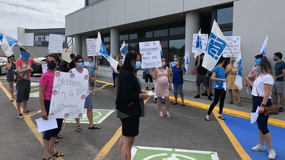 Des infirmières manifestent avec des pancartes à la main dans un stationnement.