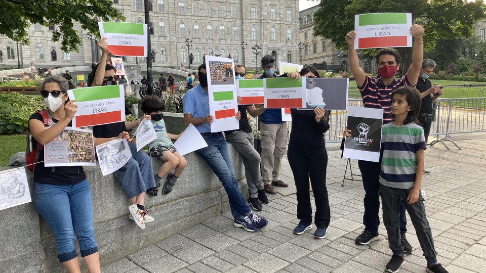 Une dizaine de personnes sont attroupées devant l'Assemblée nationale de Québec et brandissent des pancartes aux couleurs du drapeau iranien, c'est-à-dire vert, blanc et rouge.