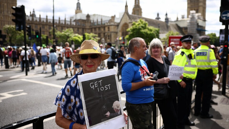 Trois manifestants près du Parlement, dont deux tiennent des pancartes.