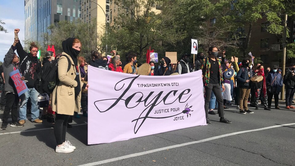 Des manifestants tiennent une banderole violette sur laquelle on peut lire : Justice pour Joyce.
