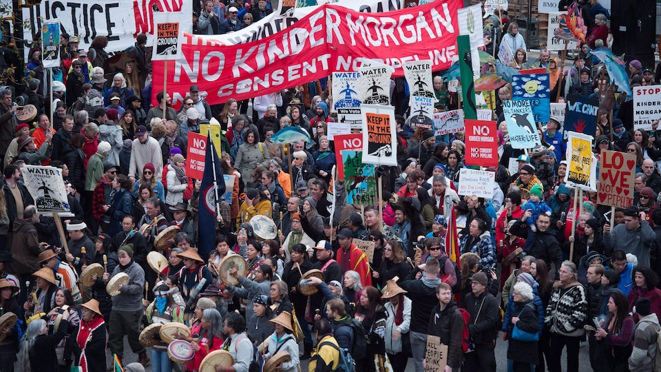 Des milliers de manifestants, certains en habits traditionnels autochtones, et plusieurs qui tiennent des pancartes sur lesquelles on peut lire an anglais Non Kinder Morgan, sont rassemblés.