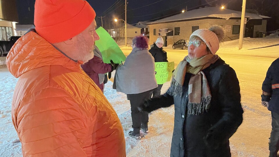 Stéphane Grenier regarde Céline Brindamour parler alors que des bénévoles manifestent près d'eux.