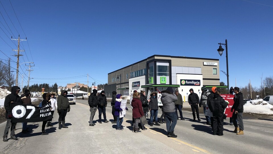 Une vingtaine de manifestants avec des pancartes à la main dans la rue devant un commerce en hiver.
