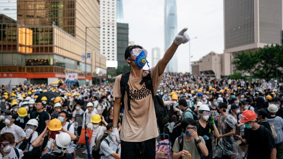 Un jeune portant un masque se tient debout, un bras levé, devant une foule de manifestants.