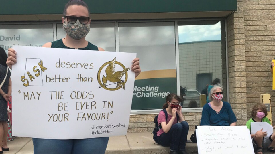 Une femme tenant une pancarte lors d'une manifestation à Saskatoon pour le port du masque dans les écoles.