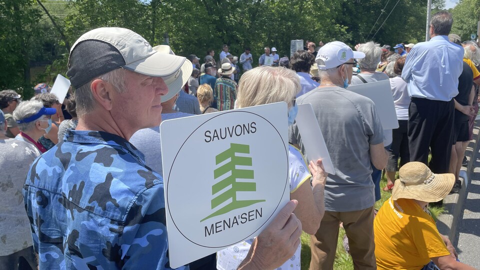 Un homme tient une pancarte qui porte la mention « Sauvons Mena'Sen ». 