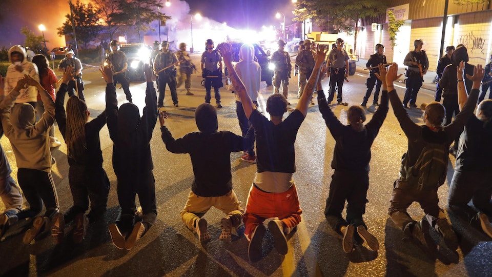 Des manifestants à genoux dans la rue, devant des policiers.
