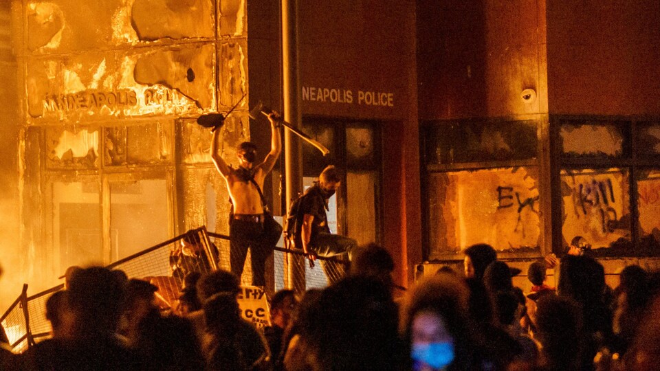 Des manifestants sont debout sur une barricade devant un poste de police qui a été incendié.