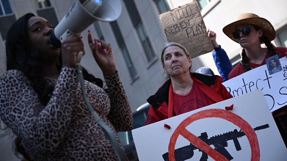 Une femme parle dans un porte-voix devant des manifestants qui brandissent des pancartes pour demander un contrôle accru des armes à feu.
