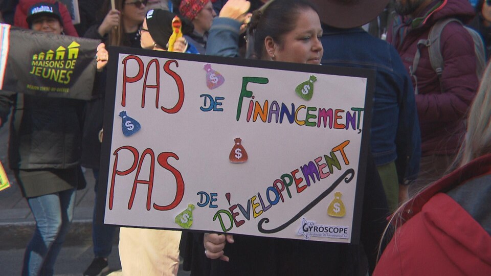 Une femme qui tient une pancarte où l'on peut lire : Pas de financement, pas de développement.