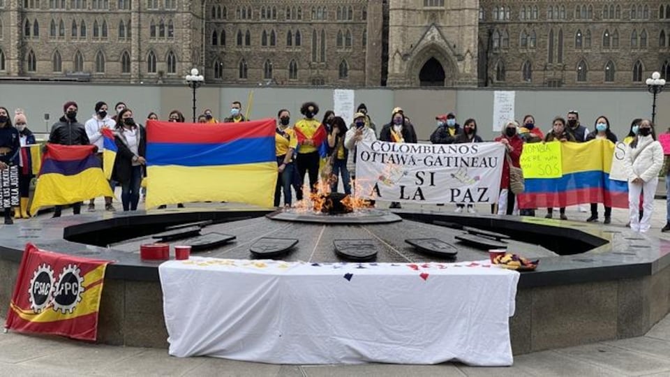 Des manifestants portants le masque brandissent le drapeau de la Colombie devant la flamme du centenaire.