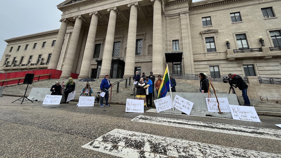 Des hommes et des femmes avec des pancartes devant le palais législatif. 