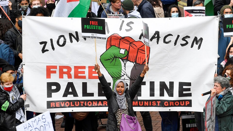 Une femme lève les bras et brandit une pancarte invitant à la libération de la Palestine. 