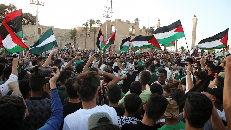 Des gens sont massés devant une mosquée et brandissent des drapeaux palestiniens. 