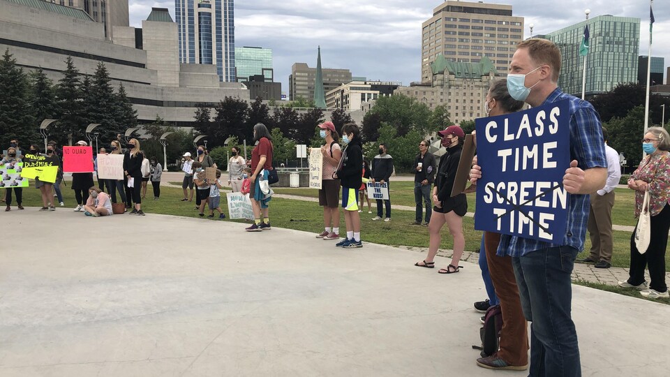 Groupe de parents dont un qui tient une affiche sur laquelle il est écrit "temps en classe".