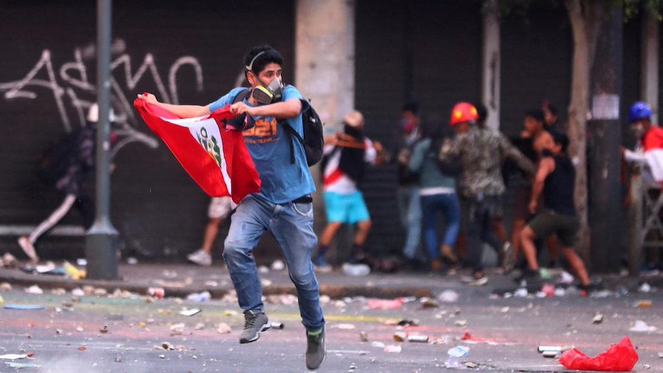 Un manifestant à Lima avec un drapeau péruvien et un masque à gaz.