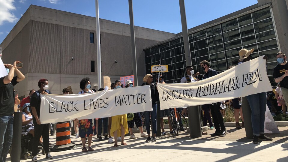 Des personnes tiennent des bannières sur lesquelles il est écrit «La vie des Noirs compte» et «Justice pour Abdirahman Abdi».