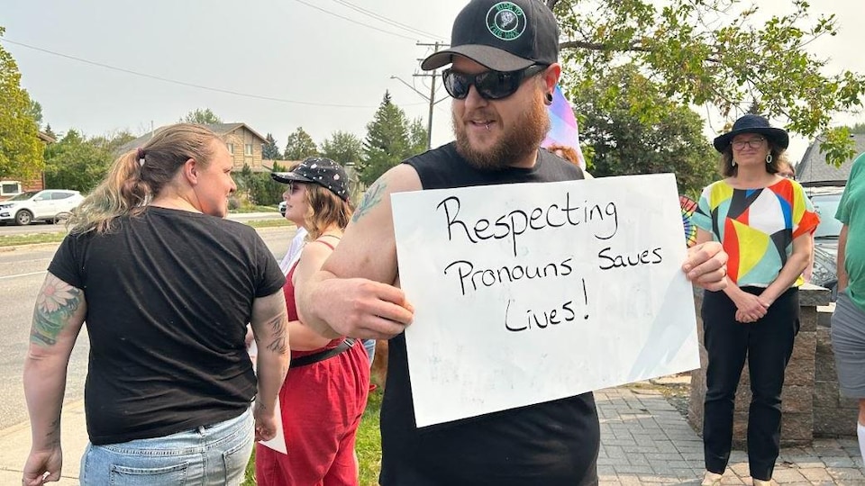 Un homme tient une pancarte avec une inscription en anglais sur le respect de l'identité de genre. 