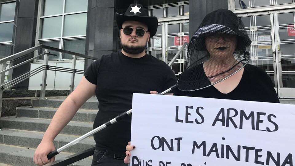 Deux manifestants vêtus de noir, pancarte à la main.
