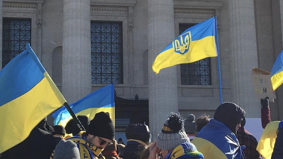 Des personnes sont rassemblées et brandissent des drapeaux de l'Ukraine.