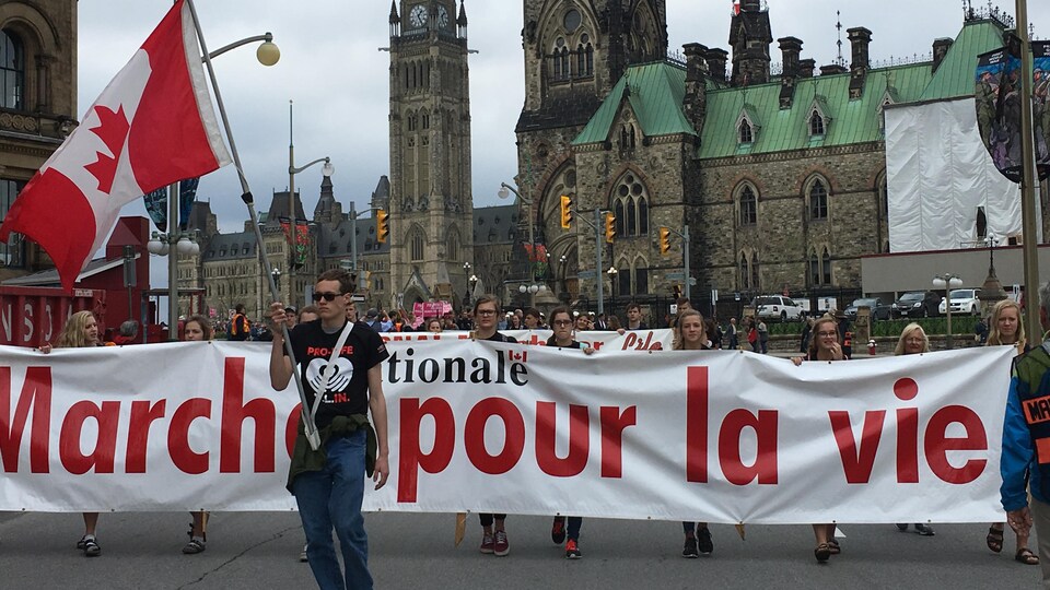 Des manifestants pro-vie marchent dans la rue à Ottawa. On peut voit une banderole où il est inscrit «Marche pour la vie» avec la tour de la Paix en arrière-plan. 