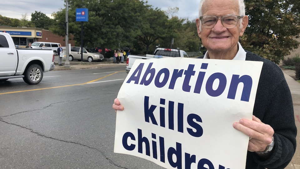 Un homme avec des lunettes tient une pancarte sur laquelle on peut lire "Abortion kills children".