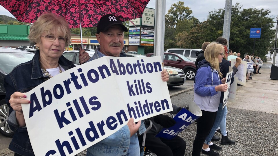 Un couple tenant des pancartes contre l'avortement et un parapluie est sur le trottoir. 