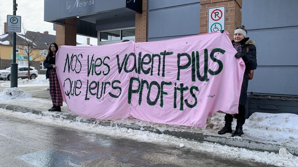 Deux manifestantes déploient une banderole sur laquelle on peut lire: Nos vies valent plus que leurs profits.