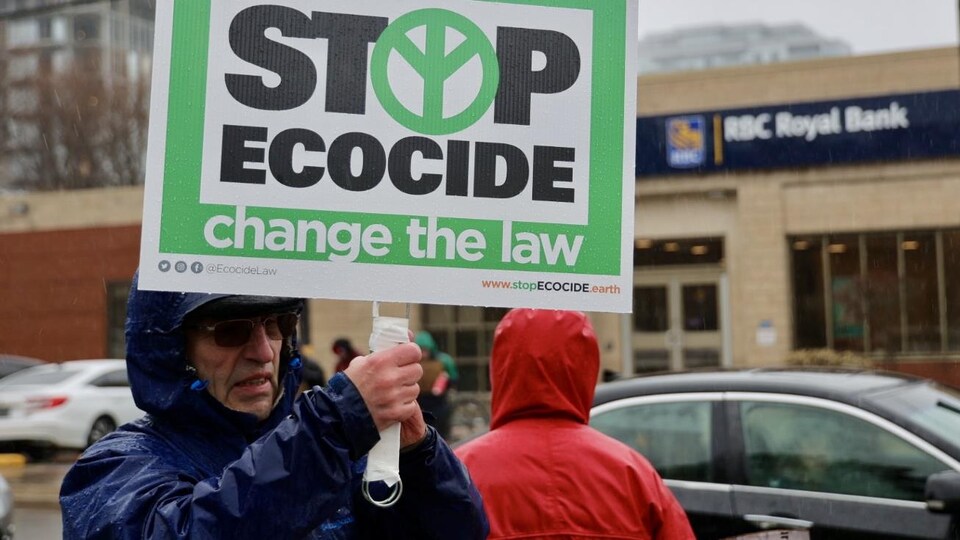 Un homme brandit une pancarte sur laquelle sont écrits les mots « Stop ecocice change the law ».