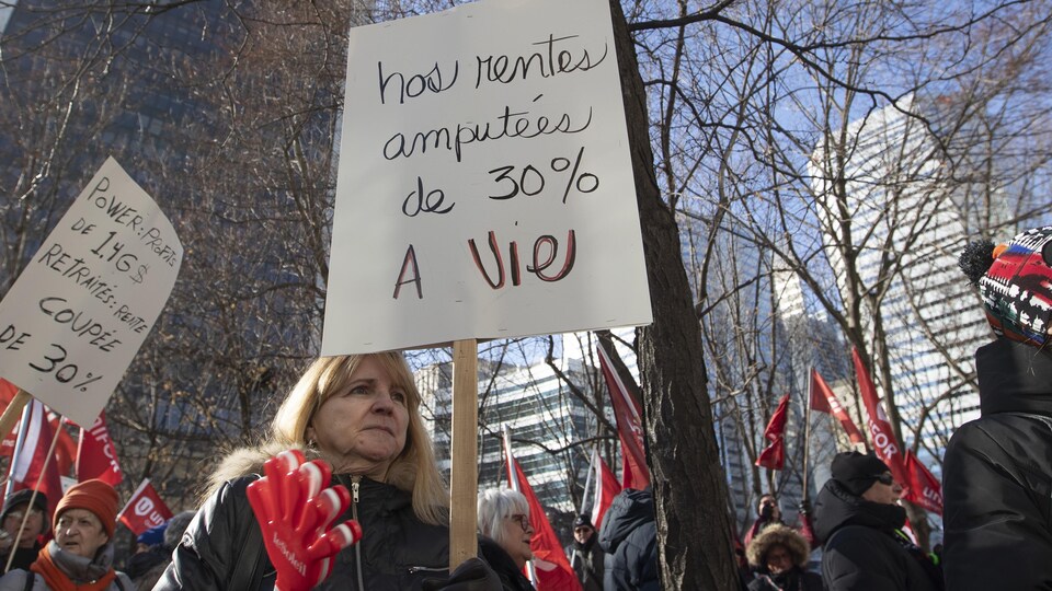 Une manifestante tient une pancarte indiquant « Nos rentes amputées de 30 % à vie » lors d'une manifestation des retraités du Groupe Capitales Médias.