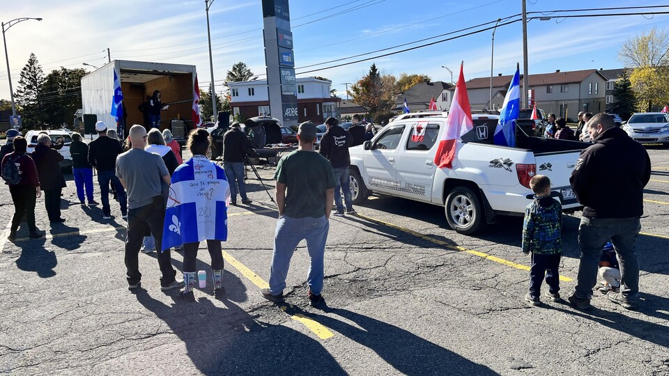 Des manifestants écoutent un discours en brandissant des drapeaux du Québec et du Canada.