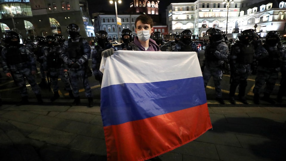 Un manifestante sostiene la bandera rusa frente a varios policías antidisturbios.
