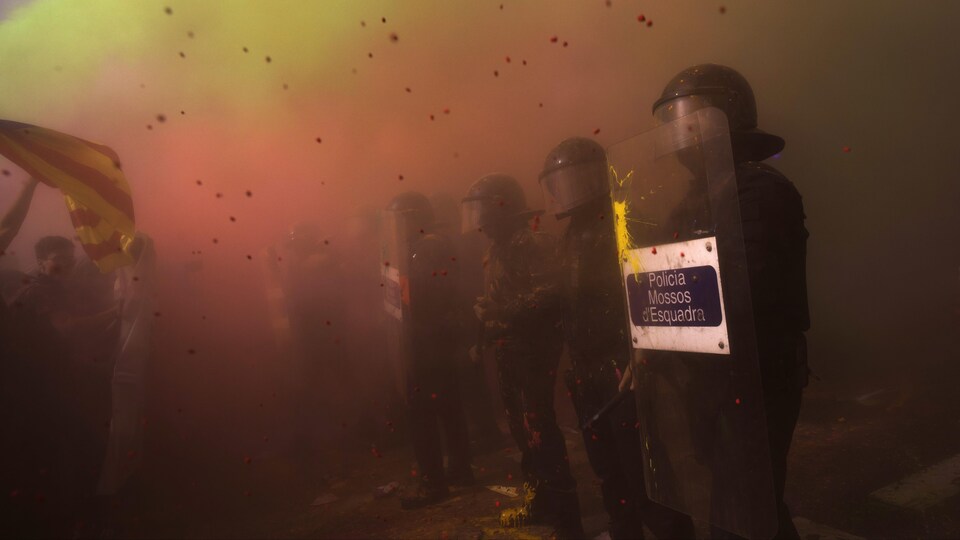 Des manifestations pro-indépendance catalane lancent de la poudre colorée à une ligne de policiers, ce qui remplit l'air ambiant d'une multitude de couleurs vives.