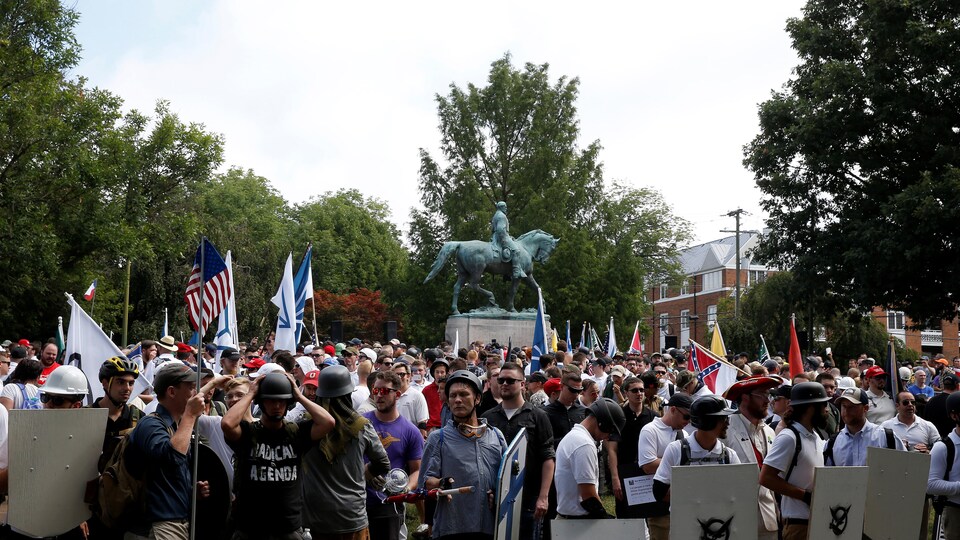Des suprémacistes blancs sont réunis au pied de la statue du général Robert E. Lee, arborant des drapeaux et des boucliers.