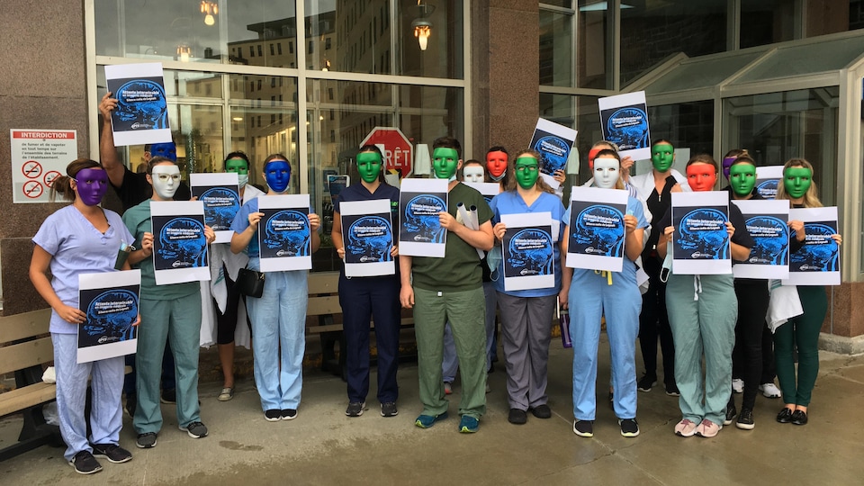 Un groupe de technologues avec un masque sur le visage manifeste à l'entrée de l'hôpital de Chicoutimi.