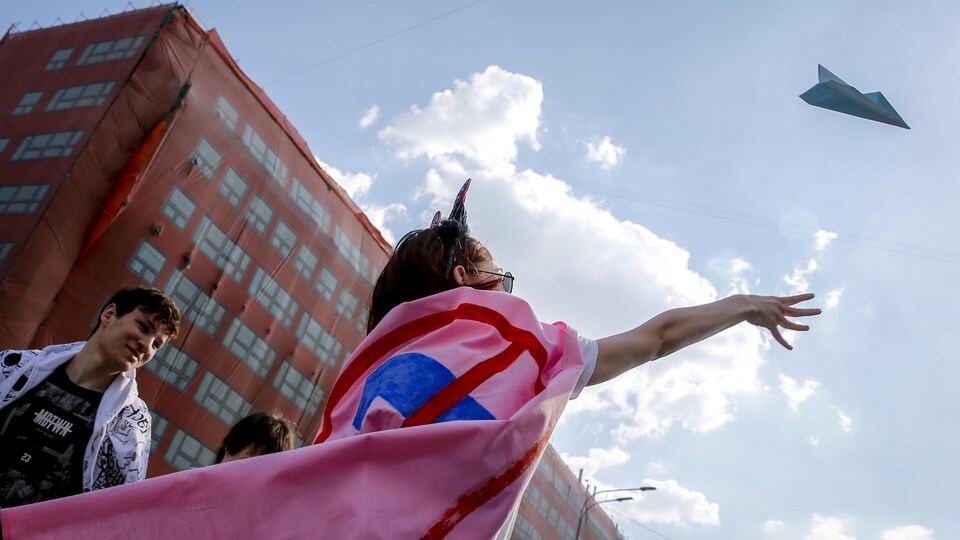 Une femme avec un drapeau rose sur les épaules lance un avion en papier. 