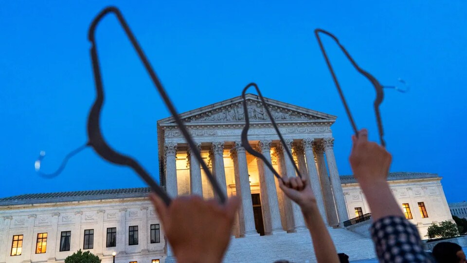 Des manifestants brandissent des cintres alors qu'ils protestent devant la Cour suprême des États-Unis, le 3 mai 2022 à Washington. 