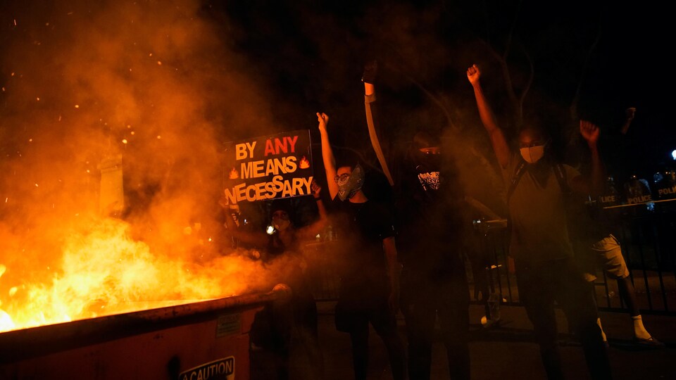 Des manifestants, le poing levé, à côté d'une structure en flammes. 