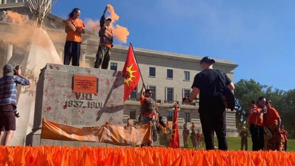Des manifestants à l'emplacement où se trouvait la statue de la reine Victoria le 1er juillet 2022 à Winnipeg.