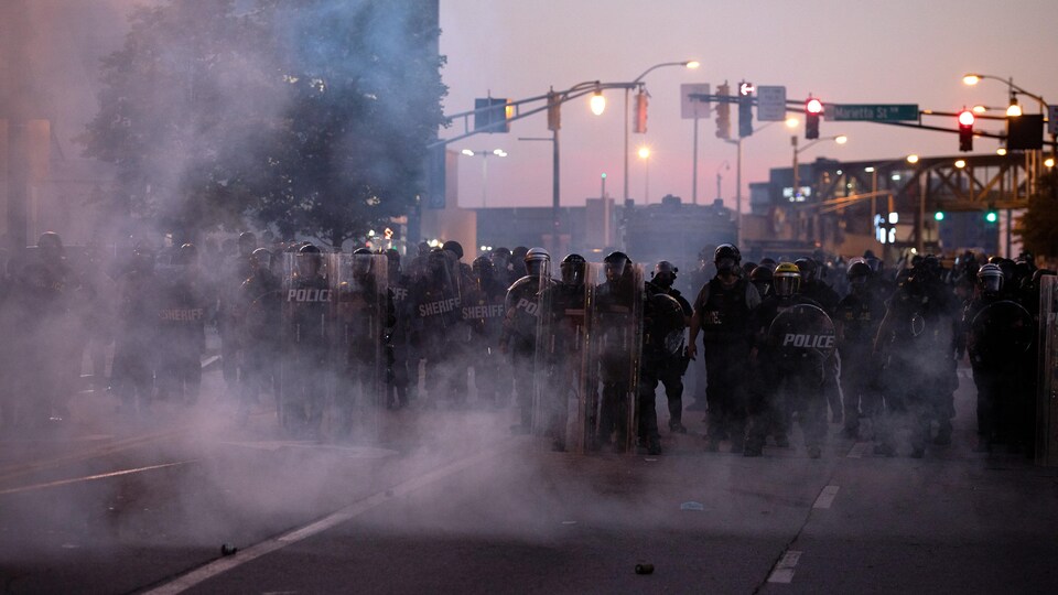 Les policiers en habits antiémeute sont entourés de gaz.