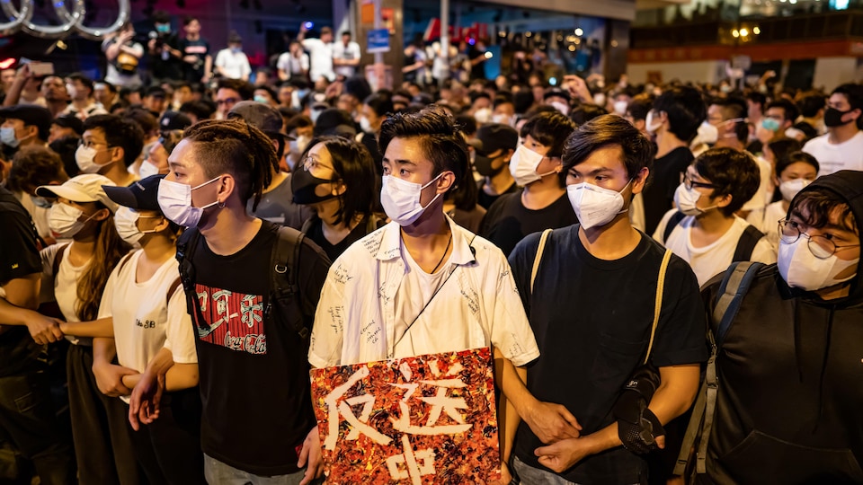 De jeunes hommes et femmes manifestent, le visage couvert par un masque chirurgical.
