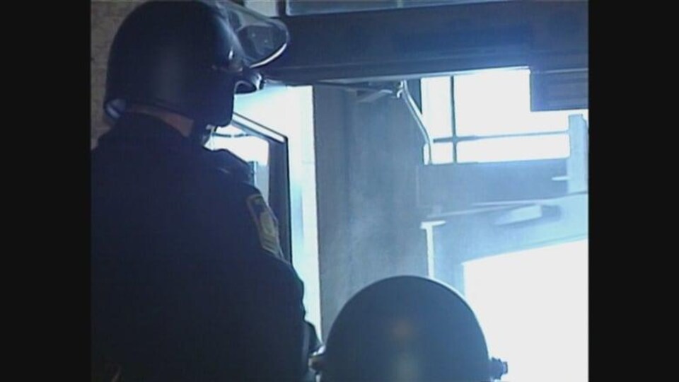 Deux agents de police portant des casques de protection devant la porte principale du palais législatif du Manitoba.