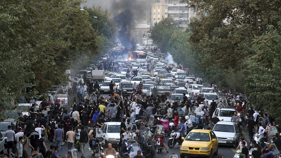 Des dizaines de voitures bloquent une rue remplie de manifestants, des feux sont allumés sur la chaussée.