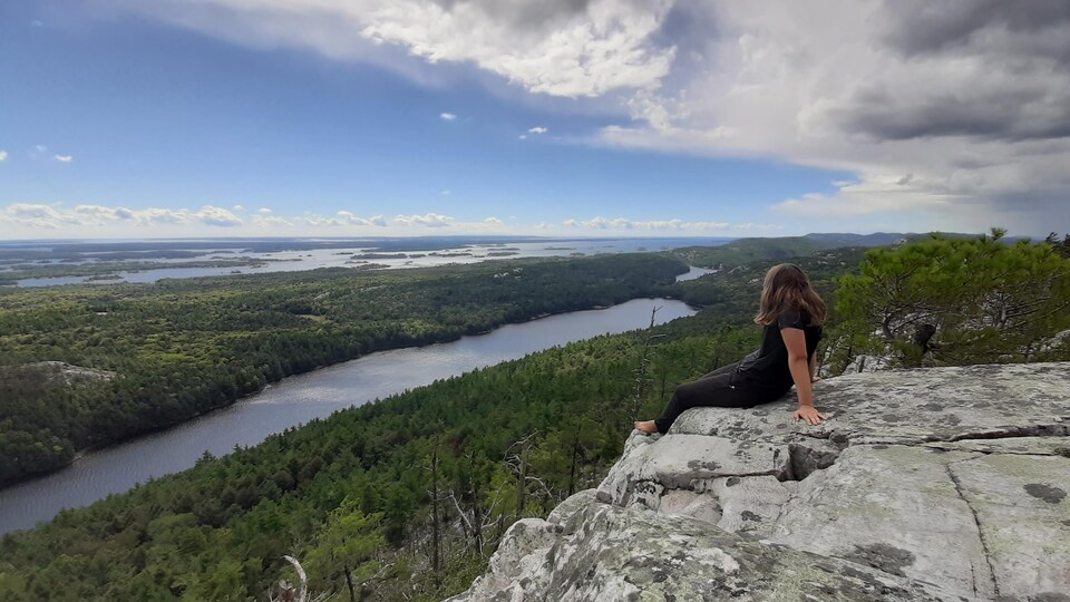 Une femme assise sur une roche admire le panorama en été