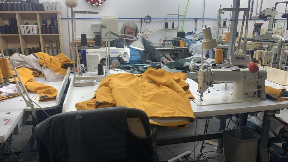 Sur une table de couture, un imperméable jaune est en préparation.
