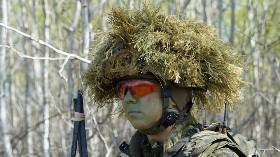 Un militaire porte un casque sur lequel est posé du matériel lui permettant de se fondre dans son environnement.